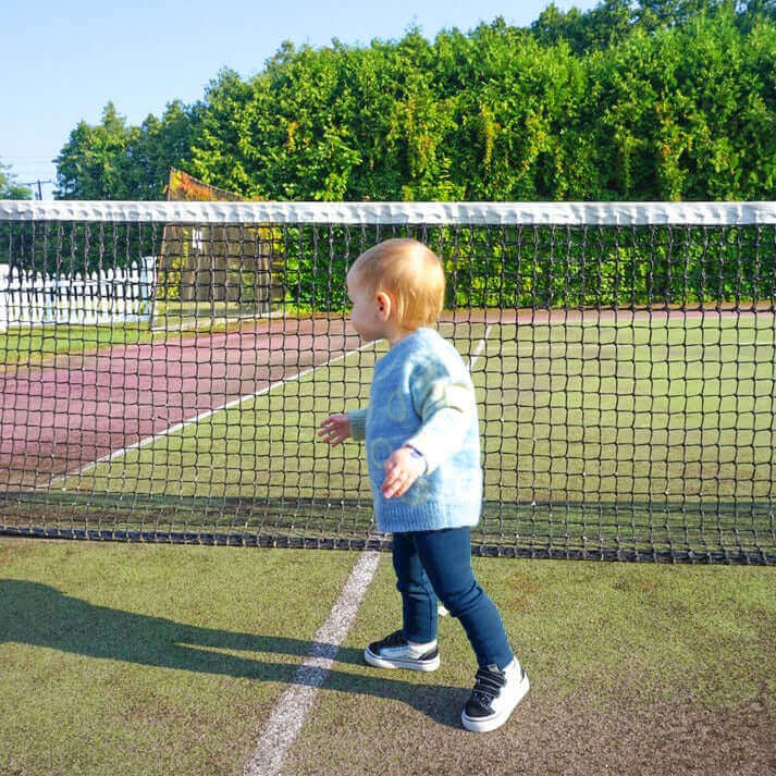 toddler on a tennis court wearing a smiley jacquard sweater and navy legging