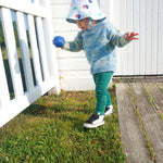 Load image into Gallery viewer, toddler walking with blue tennis ball wearing smiley jacquard sweater, printed bucket hat and green organic cotton leggings
