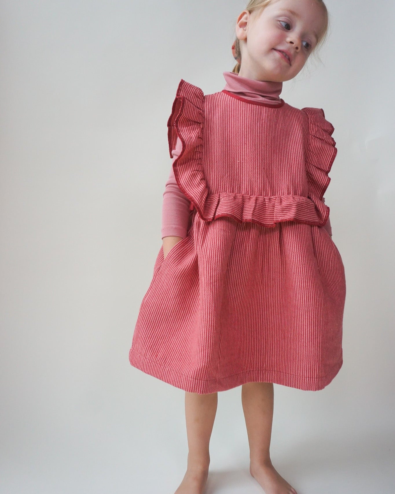 Young girl wearing a red organic cotton dress with ruffled details against a plain background
