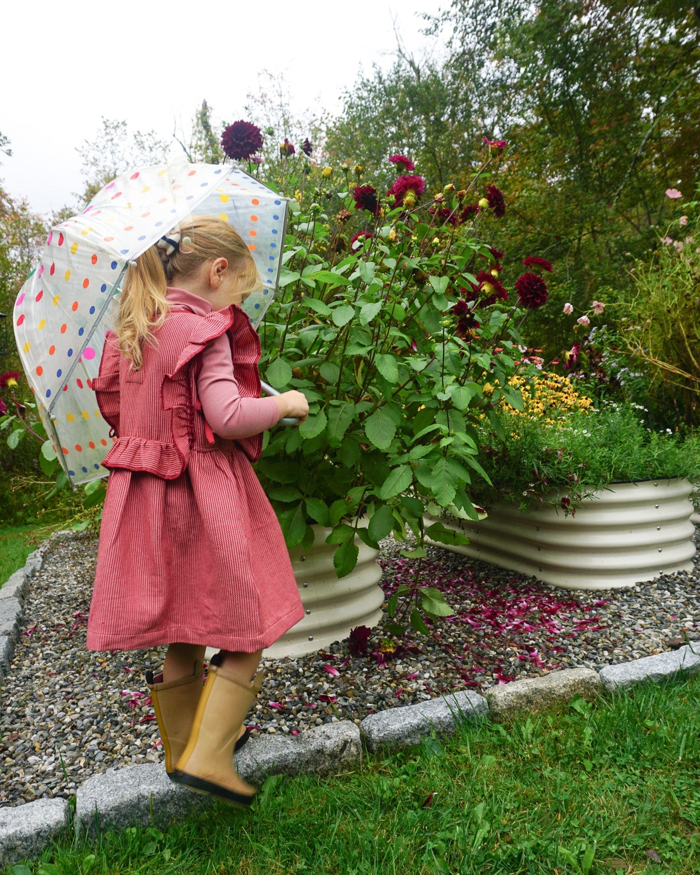Child in a pink dress with a polka dot umbrella in a garden