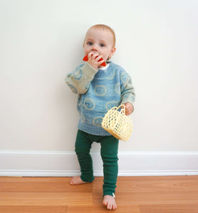 toddler wearing smiley jacquard knit sweater made from silk, mohair and alpaca and green organic cotton rib leggings