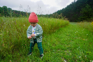 toddler wearing green marbled cardigan and green leggings walking down a grass path