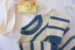 Load image into Gallery viewer, ivory and indigo blue organic cotton chunky striped sweater laying on background with sleeves folded and a yellow wooden toy camera sitting next to the sweater on the background
