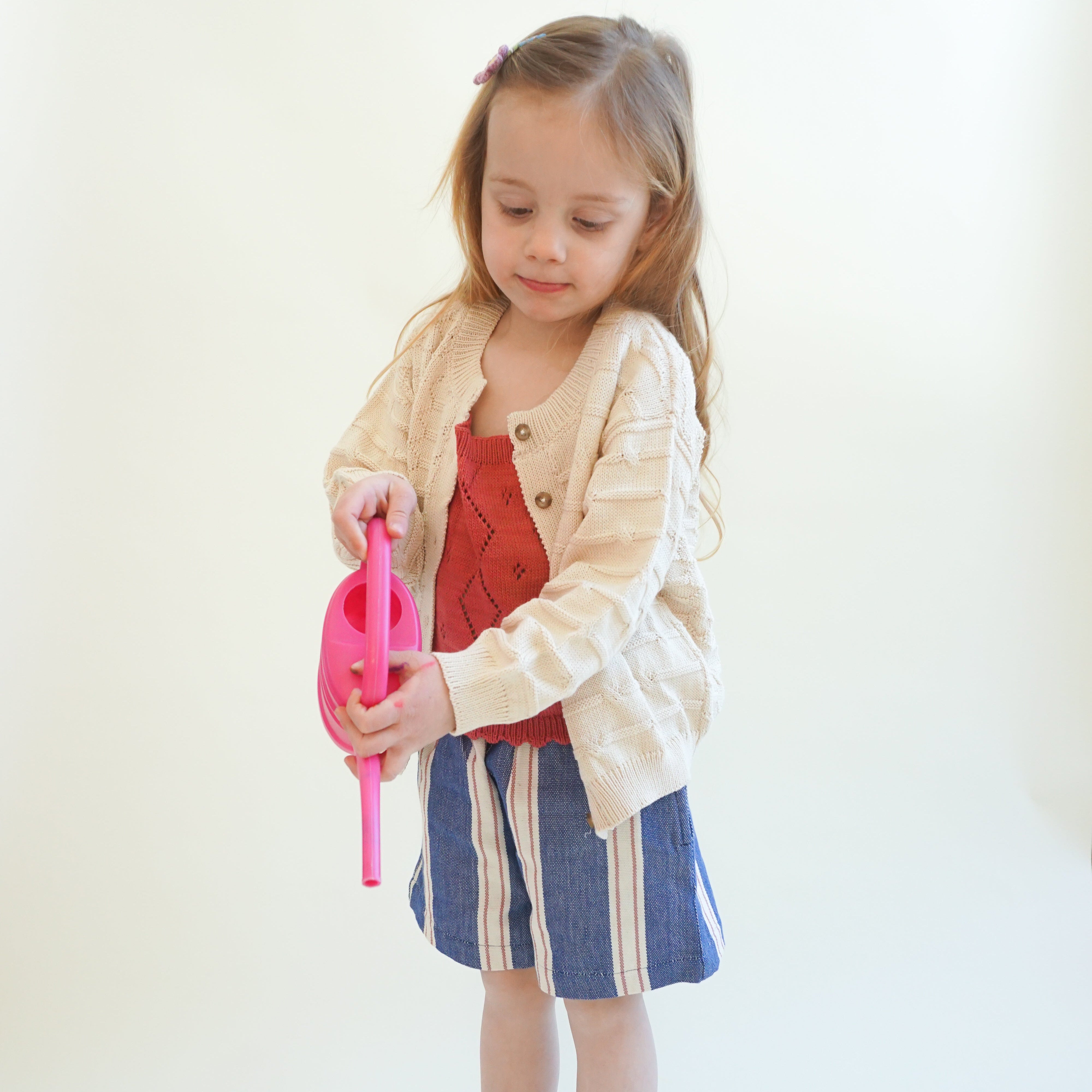 toddler wearing ream mixed stitch organic cotton baby cardigan with buttons and blue shorts with a red tank