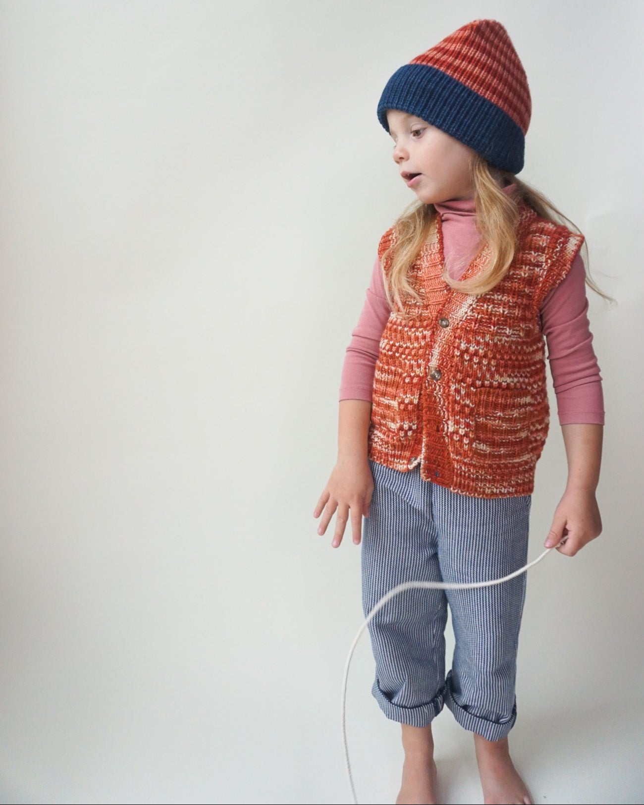 Child wearing a red patterned vest and blue knit hat on a white background