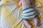 Load image into Gallery viewer, Back view of a baby laying on a yellow and cream striped blanket, wearing only an ivory and indigo blue striped organic cotton chunky knit bloomer short.
