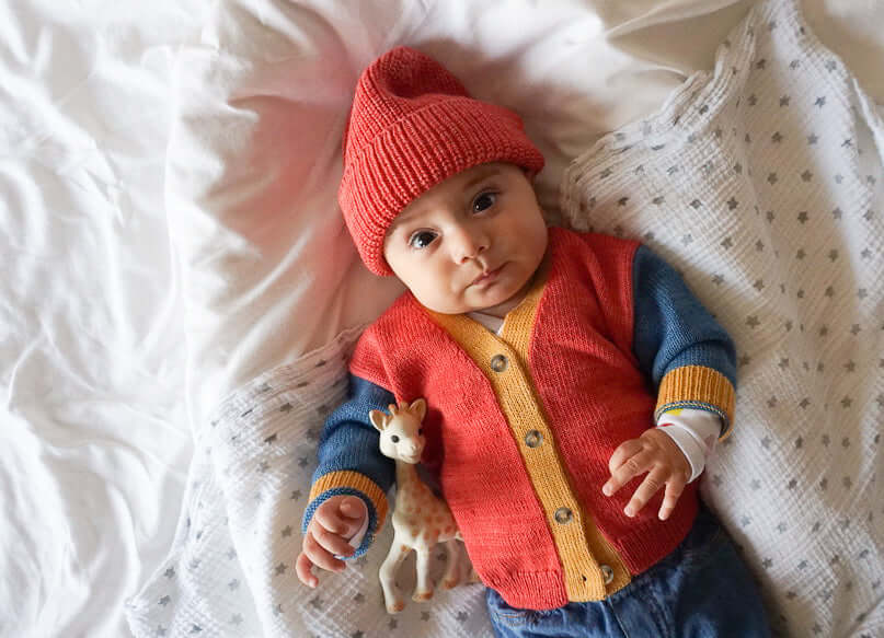 baby in red hat and colorblocked cardigan laying on a star blanket