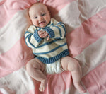 Load image into Gallery viewer, smiling baby, laying on a pink striped blanket, wearing an organic cotton chunky ivory and indigo blue striped sweater and a diaper, clapping their hands together.
